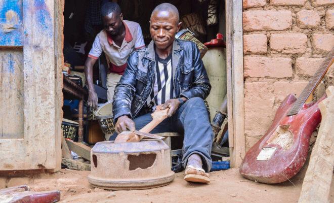 Moise Muhindo Kisuba builds a guitar at his workshop in Kirumba, south Lubero territory of the Democratic Republic of Congo. Behind him, Egide Kasereka Kighoma, an apprentice, works on a drum on July 15, 2021. Credit: Zita Amwanga/Global Press Journal.