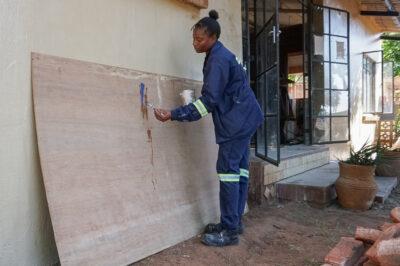 Charity Nyoni, one of the growing number of women in Zimbabwe’s construction industry, tests paint on a board in a Victoria Falls showroom. Credit: Fortune Moyo/Global Press Journal.