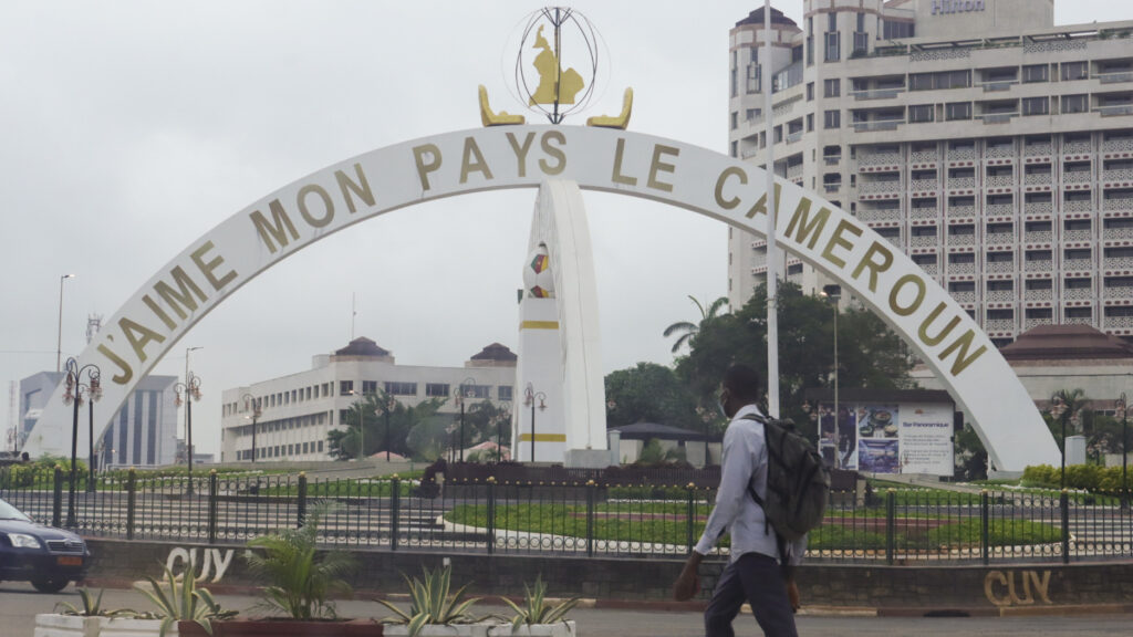 A pedestrian strolls around the monument, “J’aime mon pays le Cameroun” (“I love my country Cameroon”), at a central roundabout in the capital Yaoundé. Not visible here, the other axis of the monument reads the same message in English, symbolizing efforts by the government to promote patriotism and unity between French- and English-speaking Cameroonians. Zane Irwin, 2022.